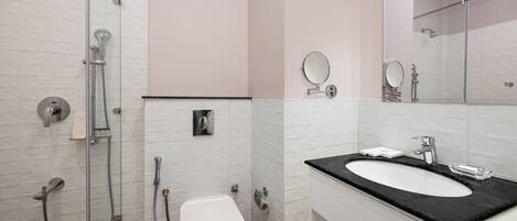 Un baño moderno con cabina de ducha de vidrio, un inodoro blanco, un lavabo negro con espejo y una pared con azulejos blancos.
