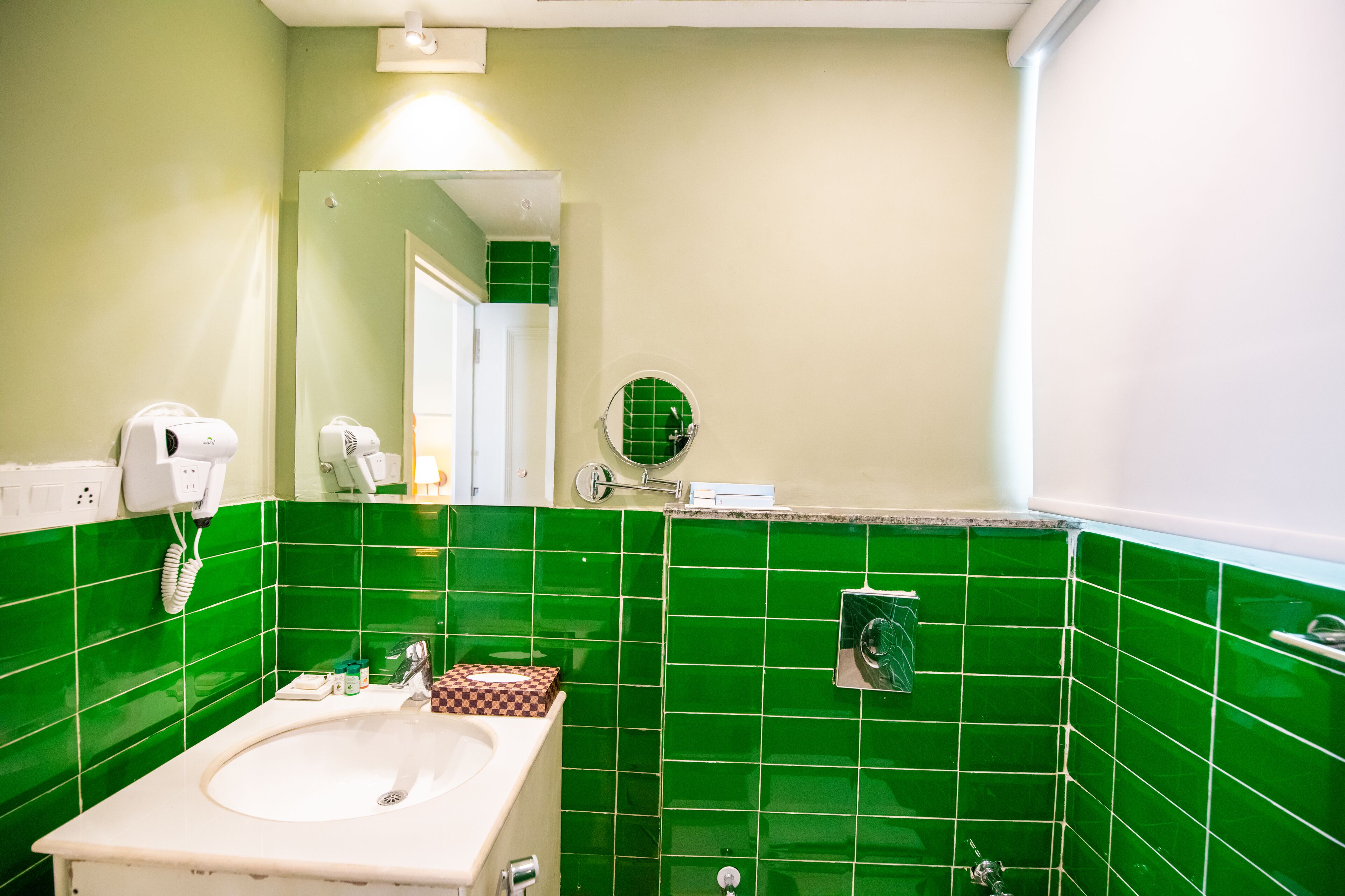Ein Badezimmer mit Waschbecken, grünen Fliesen, einem Spiegel und einem Föhn.