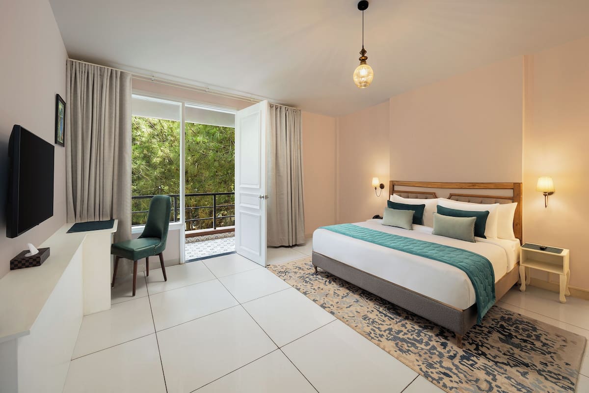 Ein modernes Hotelzimmer mit einem großen Bett, einem Schreibtisch mit Stuhl, einem Fernseher und einem Balkon mit Vorhängen.