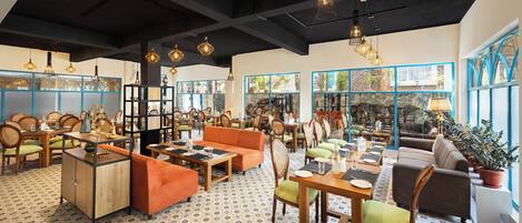 A spacious restaurant with high ceilings, exposed beams, and a mix of wooden and upholstered seating. Large windows offer views of the outdoors.