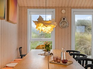 A wooden dining table with a hanging leaf-shaped light fixture, a clock, and a view of greenery outside.