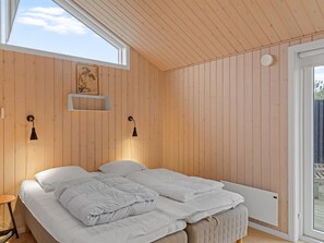Un dormitorio con techo de madera, una cama con ropa blanca, dos lámparas de pared y un ventanal.