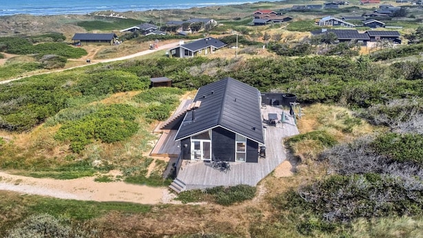 A coastal house with a deck, surrounded by dunes and ocean views.