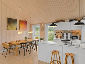 Une cuisine moderne avec des meubles blancs, un îlot central doté de tabourets, un éclairage suspendu et un coin repas avec une table et des chaises en bois.