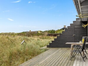 Een houten terras met een tafel en stoelen, dat uitkomt op een zwarte trap.