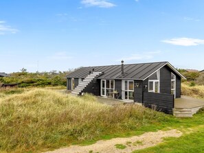 Une maison moderne aux murs noirs, dotée d’un escalier menant à une terrasse, et entourée d’une végétation luxuriante.