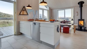 A modern kitchen with a central island, large windows, and a wood-burning stove.