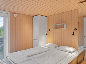 Une chambre à coucher moderne avec un plafond en bois, un grand lit avec une literie blanche et deux lampes fixées au mur.