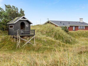 Une structure en bois avec un petit porche, un bâtiment rouge doté d’un toit en pente et un paysage verdoyant.