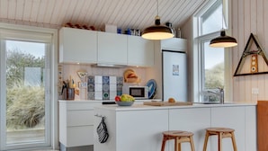 A modern kitchen with white cabinets, a central island, two wooden stools, and pendant lighting.