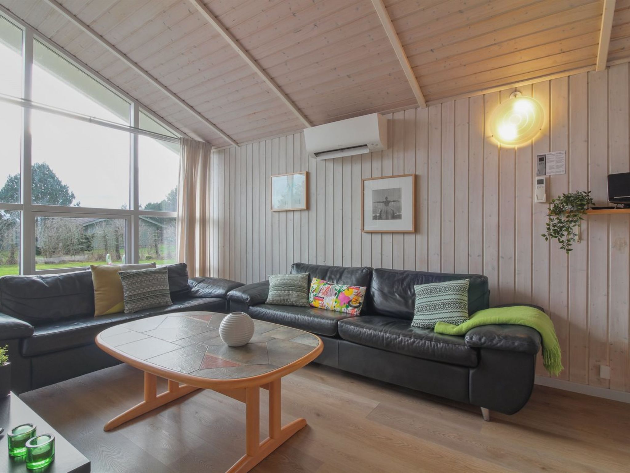 Ein modernes Wohnzimmer mit einer Ledersofa, einem runden Couchtisch und einem großen Fenster mit Blick ins Freie.
