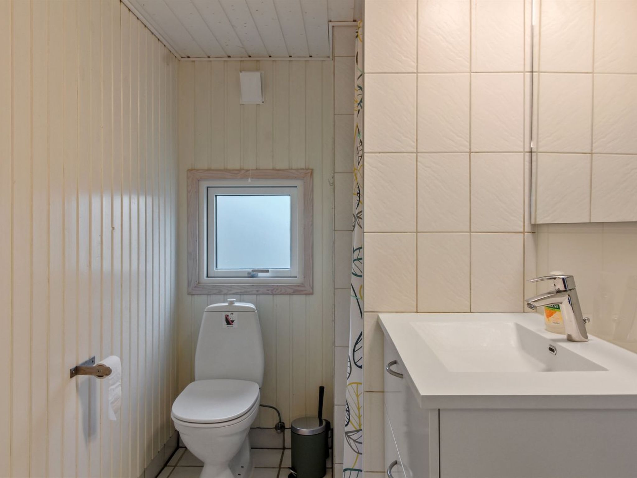 A small, clean bathroom with a toilet, a window, and a sink.