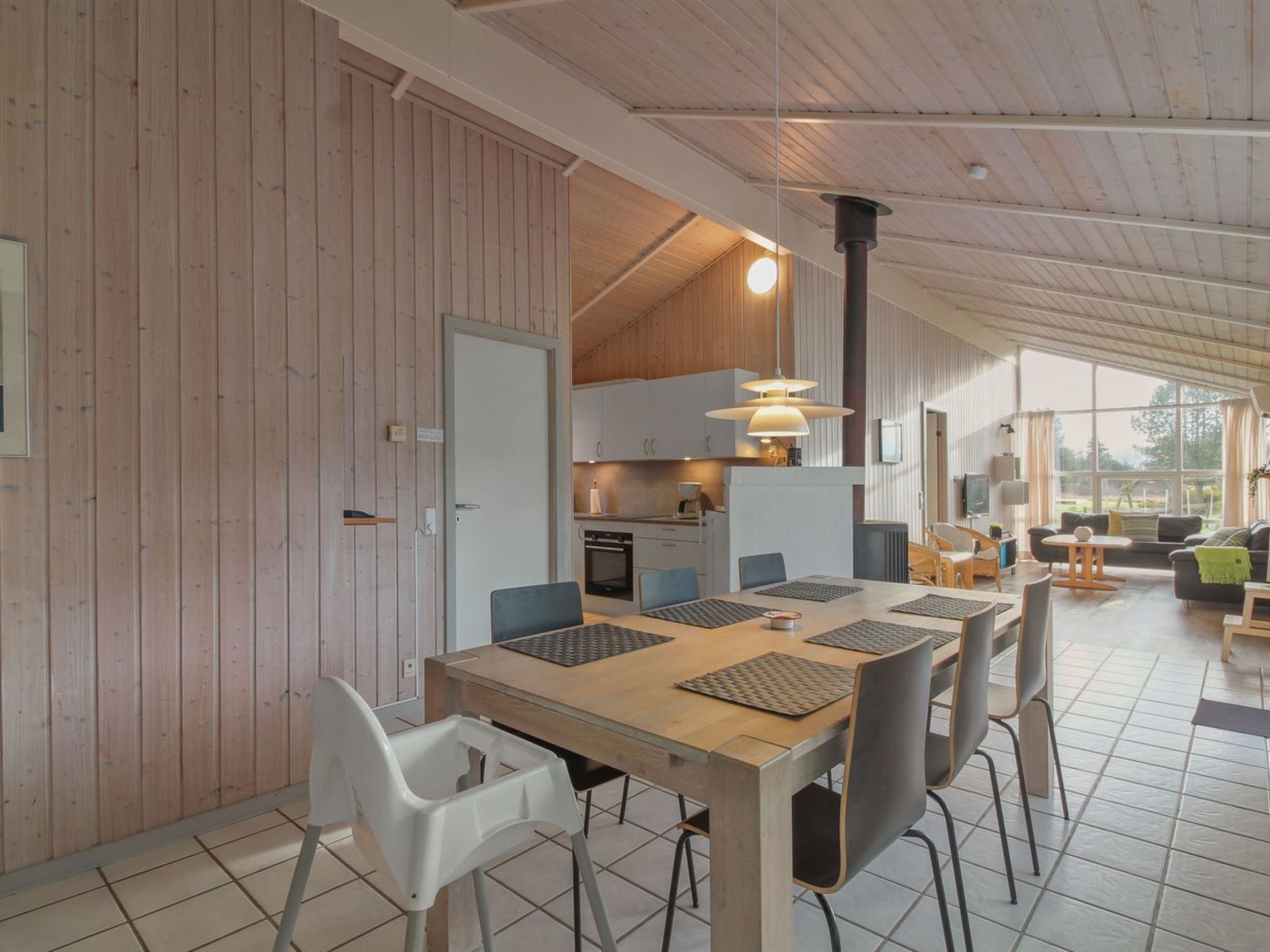 A modern interior with a wooden dining table, chairs, and a kitchen area with a stove and cabinets.