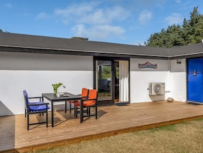 A modern building with a blue door, a table with chairs, and an air conditioning unit.