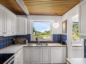 A modern kitchen with white cabinets, a wooden ceiling, a window with a view of greenery, and a Bosch dishwasher.