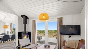 Una habitación con chimenea, televisión, zona de comedor con sillas, sofá y vista a la playa.