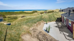 Una propiedad costera con zona arenosa, un patio con mobiliario exterior y vistas al océano.