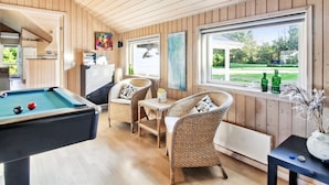 Une pièce chaleureuse avec une table de billard, des fauteuils en osier et une vue sur l’extérieur.