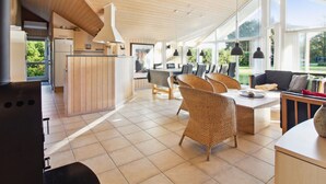 Une cuisine moderne avec des meubles en bois, un coin repas avec des chaises en osier et de grandes fenêtres donnant sur l’extérieur.