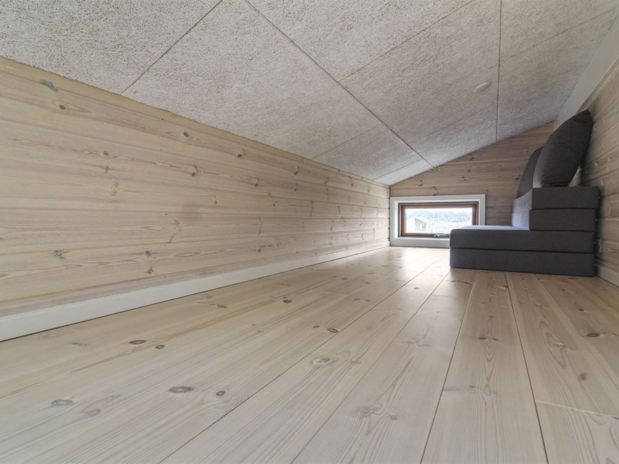 Ein Zimmer mit Holzböden und -wänden, einer schrägen Decke und einem Fenster.
