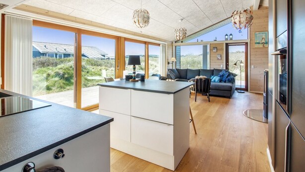 Eine moderne Küche mit Kochinsel, ein Essbereich mit einer Couch und Blick ins Freie.