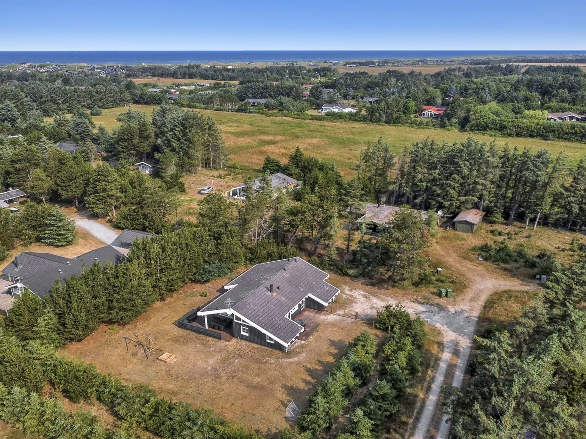An aerial view of a residential area with houses surrounded by dense forests and a clear view of the ocean.