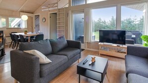 A modern living room with a sofa, a coffee table, and a TV. There is a dining area with a table and chairs, and a kitchen area with a stove. - "Kragh" - 950m from the sea by Interhome (Løkken)