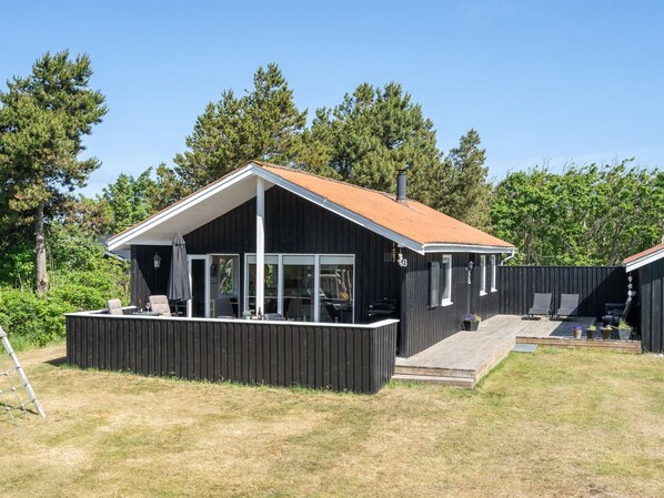 A modern black building with a sloped roof, large windows, and a covered outdoor seating area.