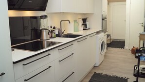 Una cocina moderna con armarios blancos, encimera negra, lavadora integrada y cafetera.