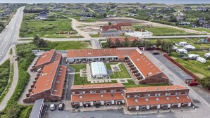 Un edificio grande y rectangular con un patio central, rodeado de zonas de estacionamiento y una carretera.