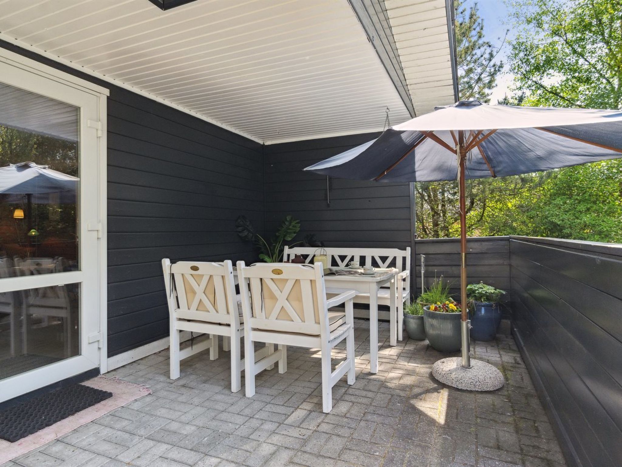 Une terrasse avec une table et des chaises, un grand parasol et des plantes en pot.