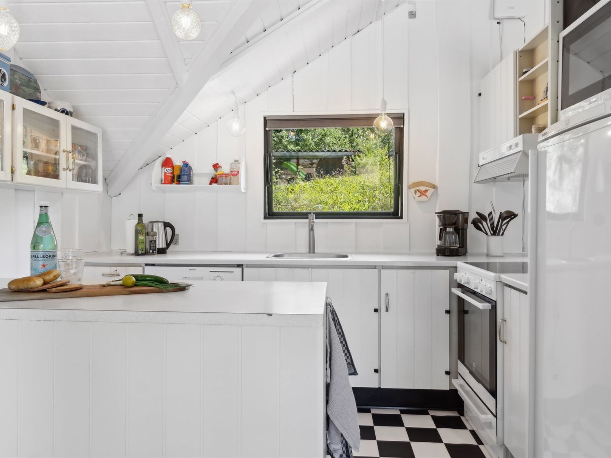 Een moderne keuken met witte kasten, een zwart-wit geruite vloer en een raam met uitzicht op groen.
