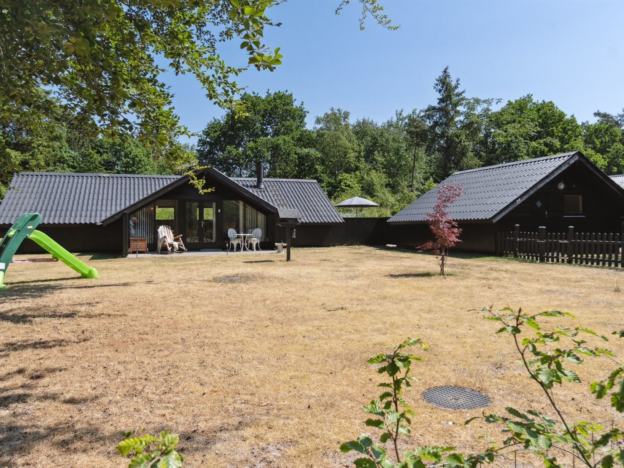 Eine rustikale Holzhütte mit einer Veranda, einem Spielbereich mit Rutsche und einem eingezäunten Garten.