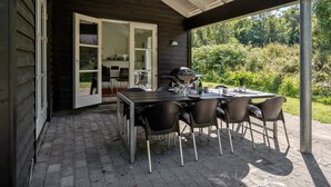 Une terrasse extérieure avec une table et des chaises, un barbecue et une vue sur la verdure.