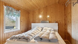 Une pièce aux murs lambrissés, avec un lit, une fenêtre avec des rideaux et un luminaire fixé au mur.