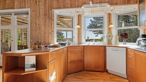 Une cuisine dotée de meubles en bois, d’un lave-vaisselle encastré et de grandes fenêtres offrant une vue sur l’extérieur.