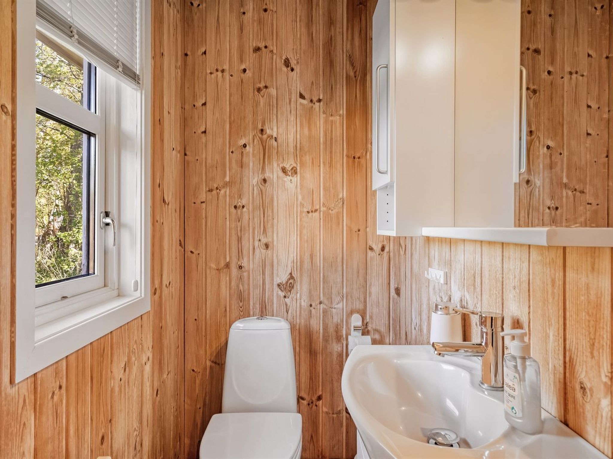Puisilla paneeleilla verhoiltu kylpyhuone, jossa on wc, pesuallas ja ikkuna.