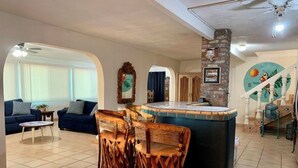 Ein Wohnzimmer mit blauem Sofa, Couchtisch und Holzstuhl. Es gibt eine Küchenzeile mit Arbeitsplatte und Spüle.