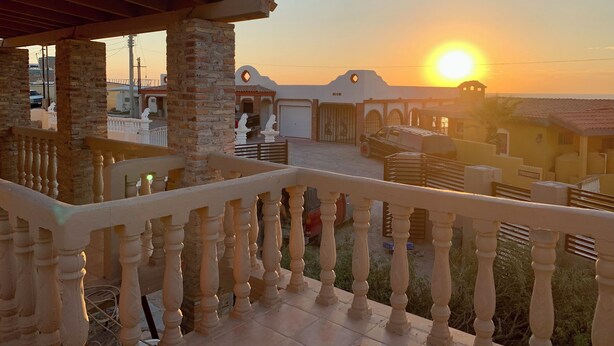 Ein Balkon mit Blick auf einen Sonnenuntergang, ein Backsteinhaus und ein geparktes Auto davor.