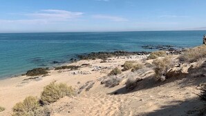 Eine Küstenlandschaft mit sandigem Strand, Felsformationen und spärlicher Vegetation.