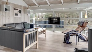 A spacious living area with a wooden ceiling, a grey sofa, a TV mounted on a wall, and a balcony with a view of trees. - "Ove" - 500m from the sea by Interhome (Hals)