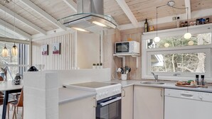 A modern kitchen with white cabinetry, a stainless steel range hood, a microwave, and a dishwasher. There is a window above the sink, and a dining area with chairs and a table. - "Ove" - 500m from the sea by Interhome (Hals)