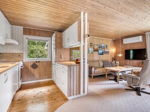 Een moderne keuken met houten kasten, een eethoek met tafel en stoelen, en een woonruimte met een bank en televisie.