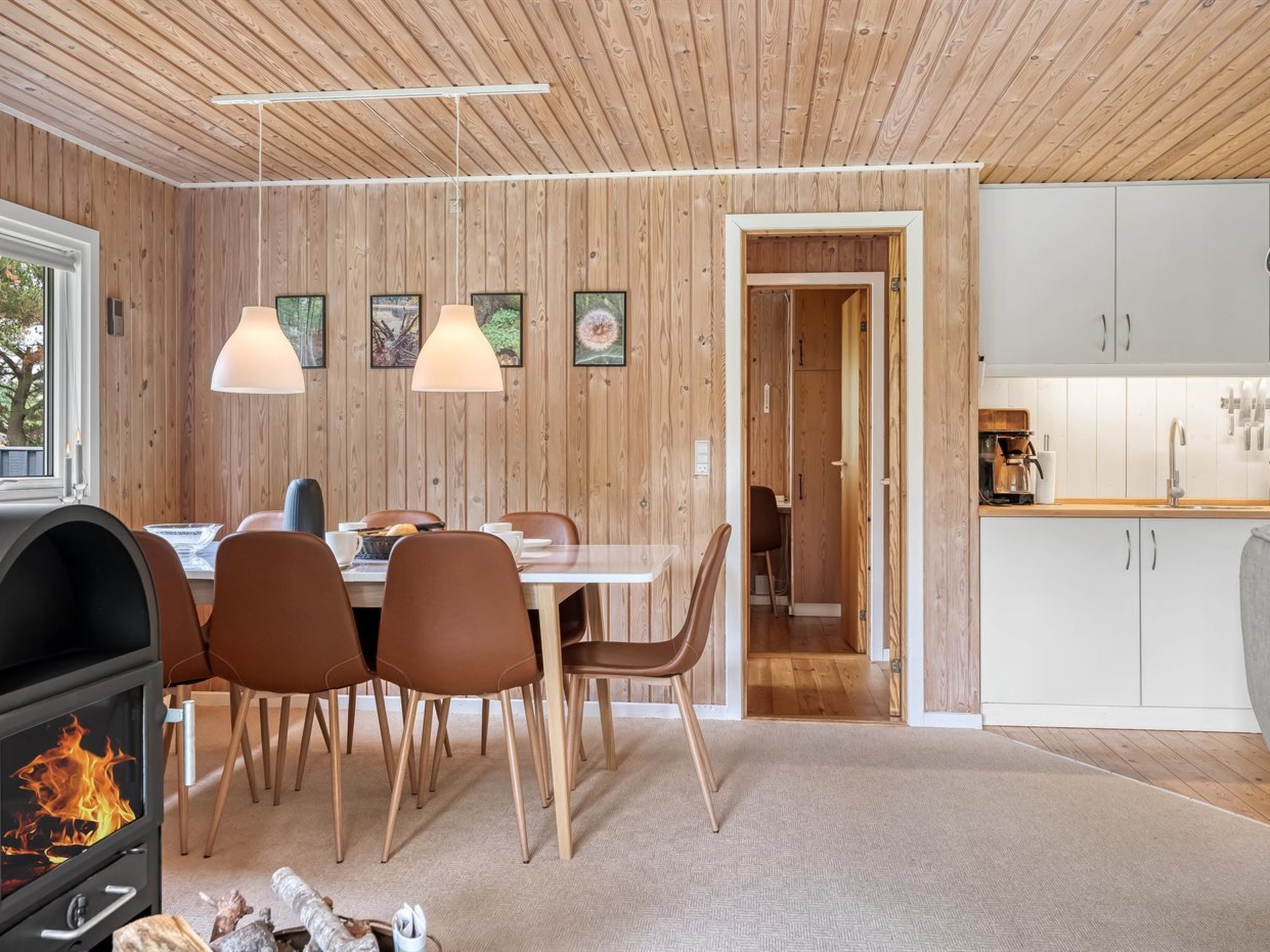 Una cocina moderna con armarios blancos, un comedor con sillas marrones y techo de paneles de madera.