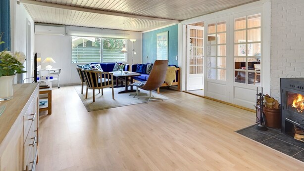A spacious living room with a wooden ceiling, a blue sofa set, a fireplace, and a view through the open door. - "Rudi" - 450m from the sea by Interhome (Hals)