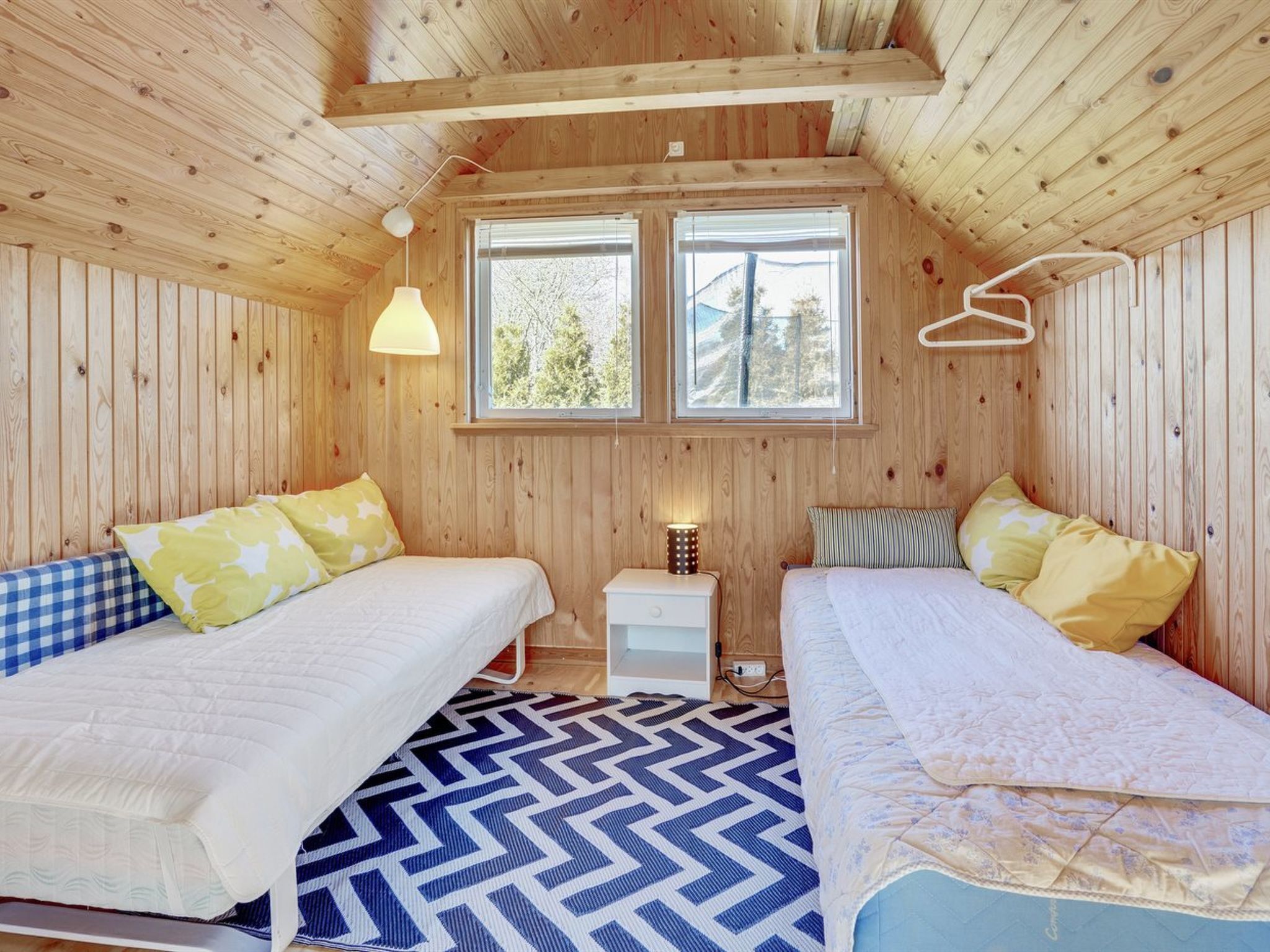 Ein gemütliches Cabin-Zimmer mit zwei Betten, einem Fenster mit Blick auf Bäume und einer Holzwanddecke.
