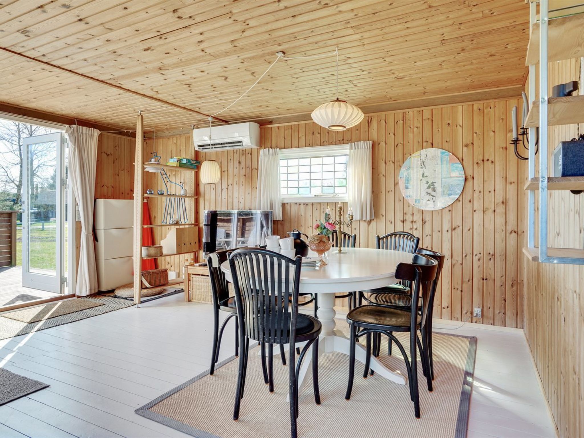 Interior de una cabaña de madera con comedor, cocina y un ventanal grande.