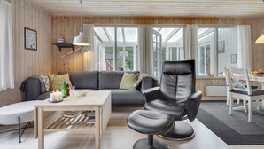 Un salon chaleureux avec un canapé gris, un fauteuil en cuir noir, une table basse en bois et un coin repas comprenant une table et des chaises blanches.