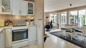 Une cuisine moderne avec des meubles blancs, une cuisinière et une machine à café. On y trouve un coin repas avec une table et des chaises, ainsi qu’une grande fenêtre qui laisse entrer la lumière naturelle.
