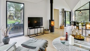 Ein modernes Wohnzimmer mit großem Fernseher, Kaminofen und Essbereich mit Tisch und Stühlen.
